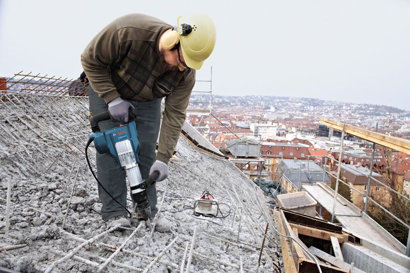 บุคคลที่สวมอุปกรณ์ด้านความปลอดภัยใช้ค้อนทุบทำลายคอนกรีตบนหลังคา.