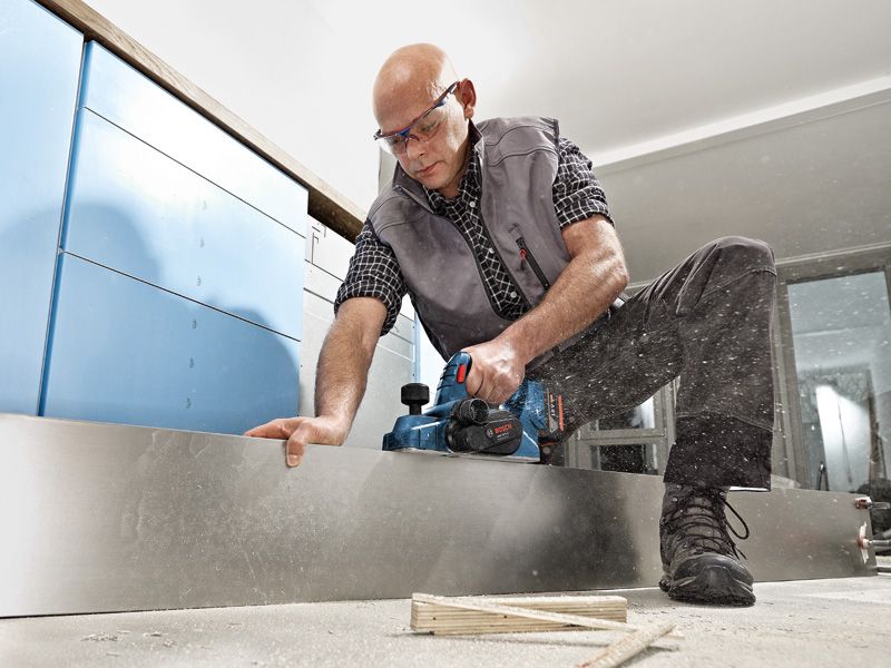 บุคคลที่สวมอุปกรณ์ความปลอดภัยกำลังไสไม้กระดานโดยใช้เครื่องไสไม้แบบไร้สาย.