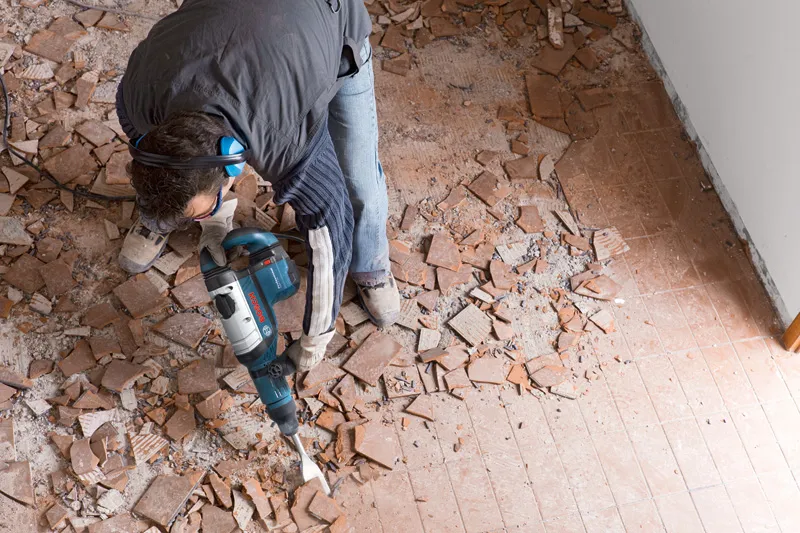 บุคคลที่สวมอุปกรณ์ความปลอดภัยทุบกระเบื้องพื้นโดยใช้ค้อนทุบทำลาย.