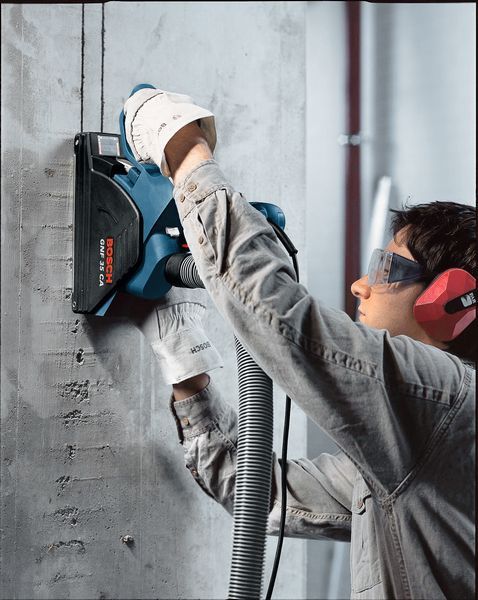 บุคคลที่สวมอุปกรณ์ด้านความปลอดภัยใช้เครื่องไล่ผนังเพื่อตัดช่องในคอนกรีต.