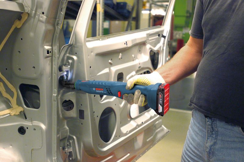 บุคคลที่สวมอุปกรณ์ด้านความปลอดภัยใช้เครื่องมือไร้สายในการยึดบานพับภายในประตูรถยนต์.