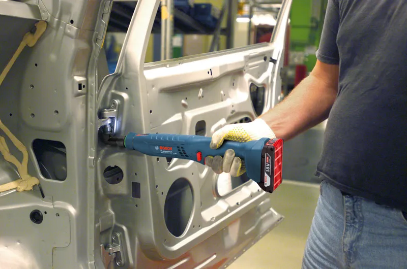 บุคคลที่สวมอุปกรณ์ด้านความปลอดภัยใช้เครื่องมือไร้สายในการยึดบานพับภายในประตูรถยนต์.