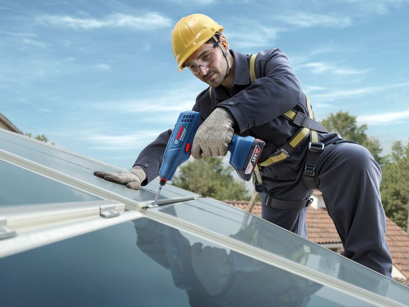 บุคคลที่สวมอุปกรณ์ด้านความปลอดภัยกำลังขันน็อตแผงโซลาร์เซลล์บนหลังคาโดยใช้เครื่องมือไฟฟ้า.