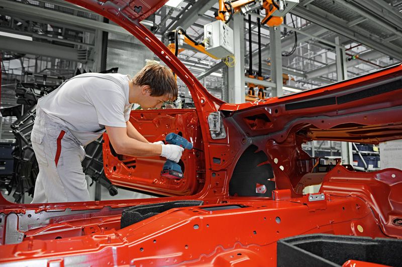 บุคคลที่สวมอุปกรณ์ความปลอดภัยใช้สว่านไร้สายในการประกอบประตูรถยนต์ในโรงงาน.