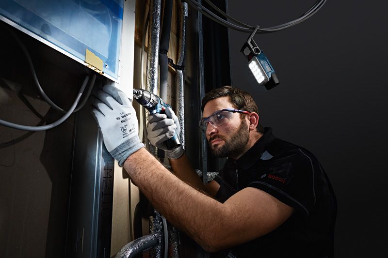 บุคคลที่สวมอุปกรณ์ด้านความปลอดภัยเจาะเข้าไปในผนังและมีแสงไร้สายส่องสว่างไปทั่วพื้นที่ทำงาน.