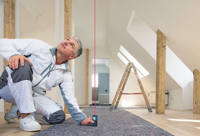 บุคคลใช้เครื่องวัดเลเซอร์เพื่อตรวจสอบการจัดแนวแนวตั้งในห้องใต้หลังคาที่มีแสงสว่าง