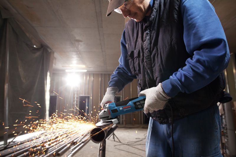 บุคคลที่สวมอุปกรณ์ความปลอดภัยกำลังบดท่อโลหะทำให้เกิดประกายไฟ.