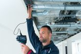 บุคคลใช้เครื่องตรวจจับเทอร์โมเพื่อตรวจสอบท่อ HVAC บนเพดาน