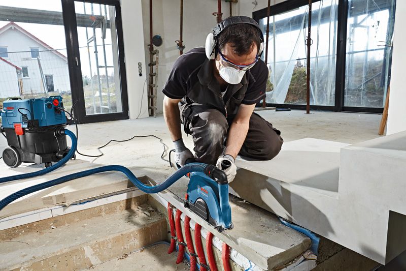 บุคคลที่สวมอุปกรณ์ความปลอดภัยกำลังตัดคอนกรีตใกล้ท่อที่โผลออกมาด้วยเครื่องตัดผนัง