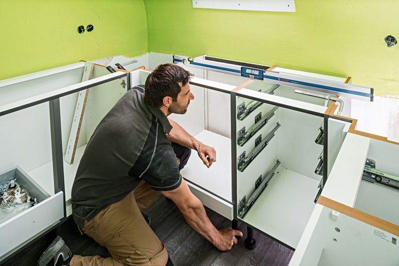 คนๆ หนึ่งกำลังติดตั้งตู้โดยใช้เครื่องตรวจวัดความเอียงแบบดิจิตอลบนเคาน์เตอร์.