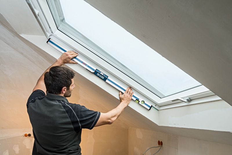 คนกำลังวัดมุมหน้าต่างด้วยเครื่องวัดความเอียงแบบดิจิตอลในห้องใต้หลังคาที่ตกแต่งเสร็จแล้ว.