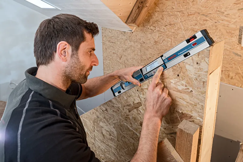 คนกำลังวัดพื้นผิวไม้ที่ทำมุมโดยใช้เครื่องวัดความเอียงแบบดิจิทัล.