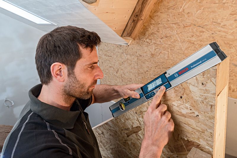 ผู้ใช้เครื่องวัดความเอียงแบบดิจิทัลเพื่อวัดมุมของโครงสร้างไม้.