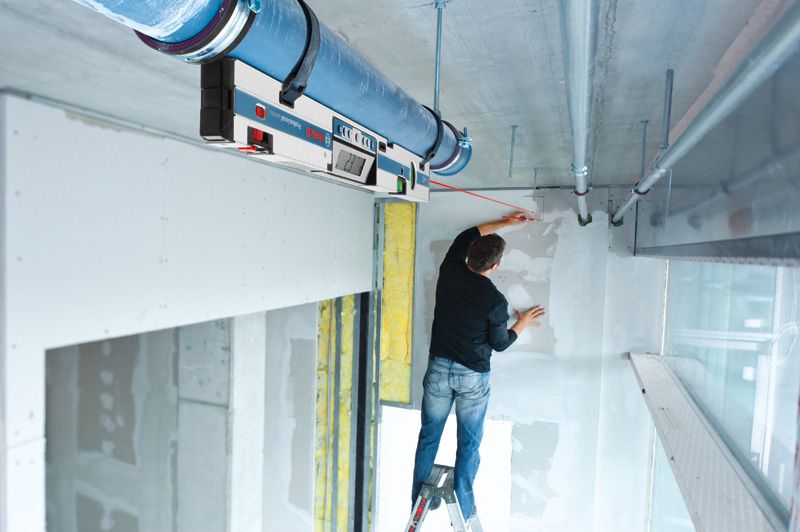 คนบนบันไดกำลังทำเครื่องหมายบนผนังโดยใช้เครื่องวัดความเอียงแบบดิจิทัลเพื่อจัดตำแหน่ง.