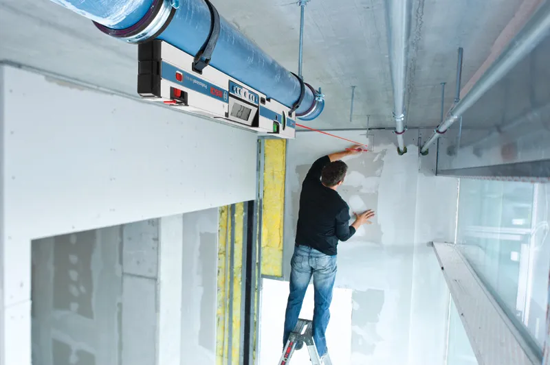 คนบนบันไดกำลังทำเครื่องหมายบนผนังโดยใช้เครื่องวัดความเอียงแบบดิจิทัลเพื่อจัดตำแหน่ง.