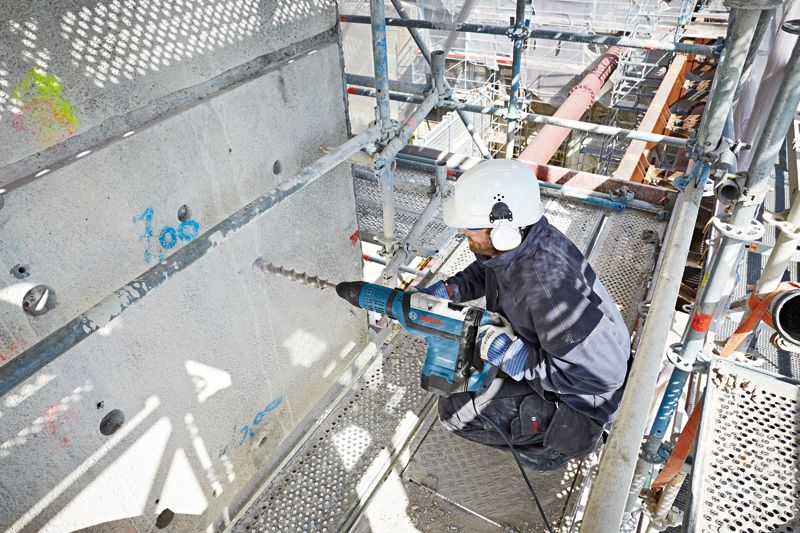 บุคคลที่สวมอุปกรณ์ด้านความปลอดภัยกำลังเจาะเข้าไปในคอนกรีตด้วยค้อนโรตารี่ขนาดใหญ่.