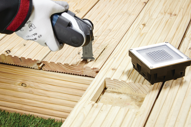 บุคคลที่สวมอุปกรณ์ความปลอดภัยใช้เครื่องมือไฟฟ้าตัดแผ่นไม้สำหรับทำพื้นระเบียง