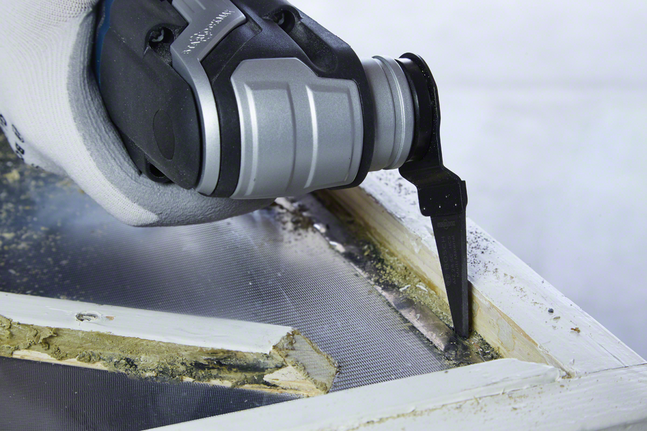 มือที่สวมถุงมือใช้เครื่องมือแกว่งตัดโป๊วกรอบหน้าต่างเก่า.