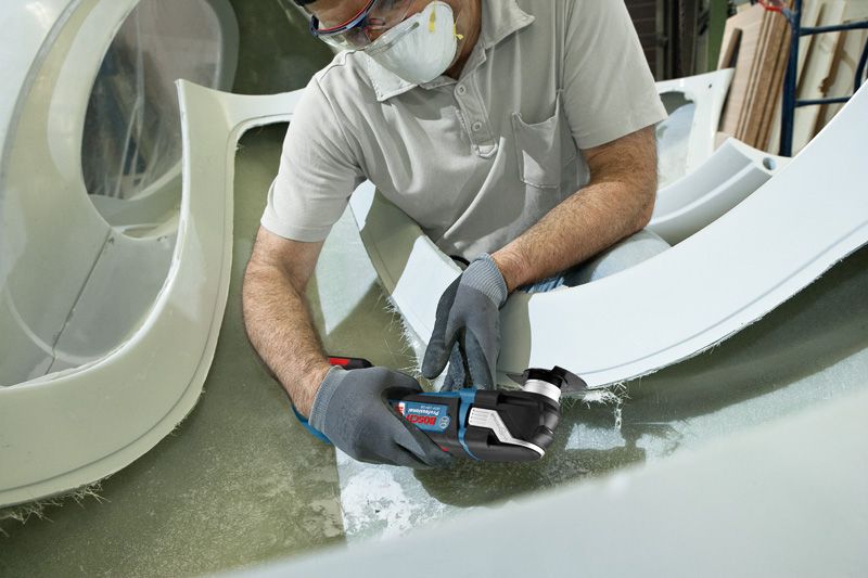 ผู้ที่สวมอุปกรณ์ด้านความปลอดภัยกำลังตัดไฟเบอร์กลาสด้วยเครื่องมืออเนกประสงค์แบบไร้สาย.