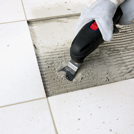 คนงานที่สวมอุปกรณ์ความปลอดภัยใช้เครื่องมือหลายประเภทเพื่อขจัดคราบกาวที่อยู่ระหว่างกระเบื้องพื้น.