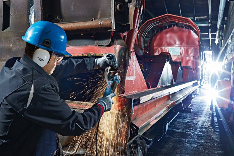 บุคคลที่สวมอุปกรณ์ความปลอดภัยกำลังบดโลหะบนรถไฟอุตสาหกรรมขนาดใหญ่.
