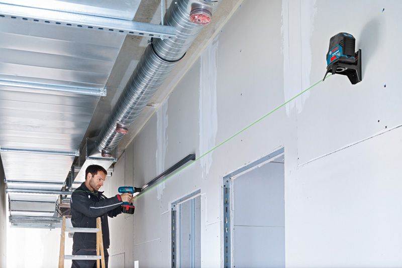 คนกำลังใช้สว่านเพื่อยึดรางโลหะ โดยมีเครื่องมือปรับระดับเลเซอร์สีเขียวเป็นแนวทาง