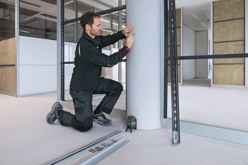 บุคคลที่สวมอุปกรณ์ด้านความปลอดภัยทำเครื่องหมายเสาคอนกรีตโดยใช้เครื่องมือปรับระดับเลเซอร์.