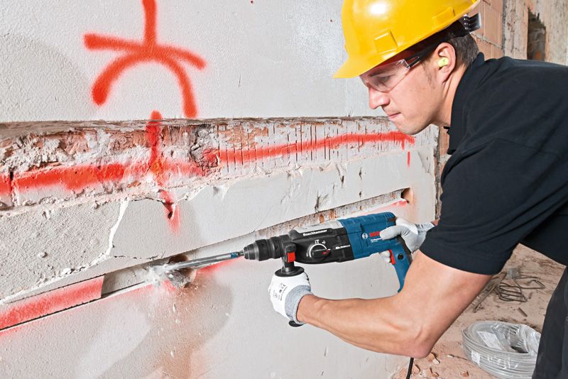 บุคคลที่สวมอุปกรณ์ด้านความปลอดภัยใช้ค้อนโรตารี่เพื่อสกัดร่องบนผนังคอนกรีต.