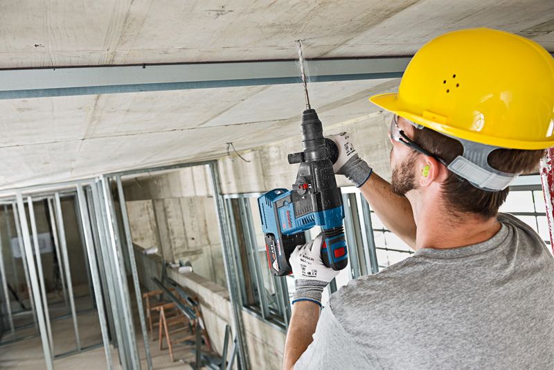 บุคคลที่สวมอุปกรณ์ความปลอดภัยกำลังเจาะเพดานคอนกรีตระหว่างการก่อสร้าง.