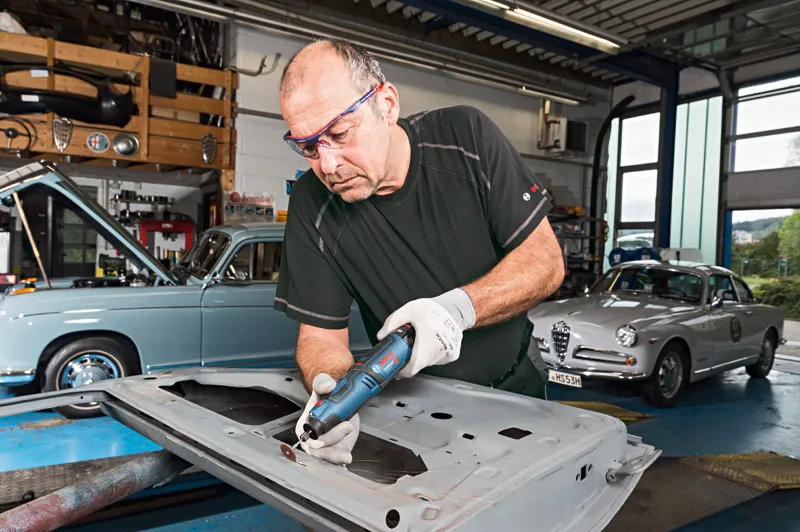 บุคคลที่สวมอุปกรณ์ด้านความปลอดภัยใช้เครื่องมือโรเตอรี่ไร้สายในการเจียรโลหะในโรงรถ.