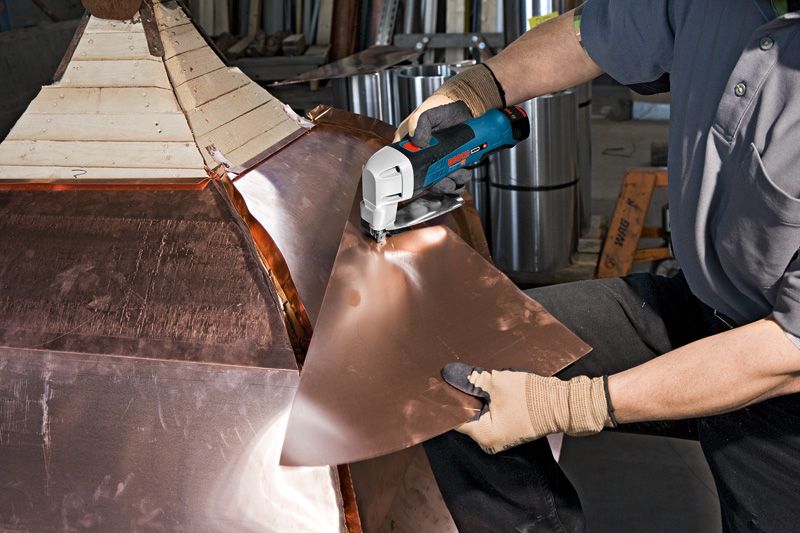 บุคคลที่สวมอุปกรณ์ด้านความปลอดภัยกำลังตัดแผ่นโลหะด้วยกรรไกรตัดโลหะแบบไร้สาย.