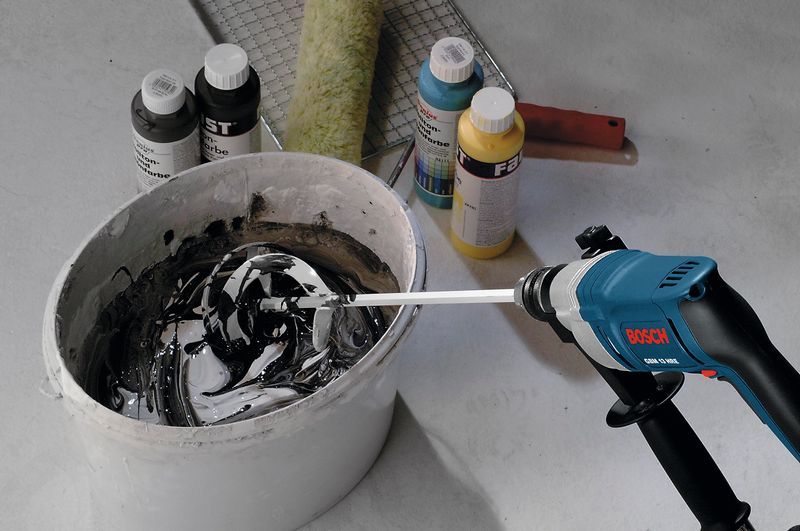 เครื่องผสมไฟฟ้าผสมสีในถังข้างๆ ขวดสีคละแบบและลูกกลิ้ง.