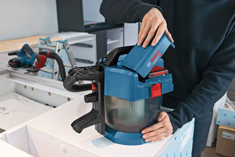 บุคคลกำลังใส่แบตเตอรี่เข้าไปในเครื่องดูดฝุ่นไร้สายบนโต๊ะทำงาน.