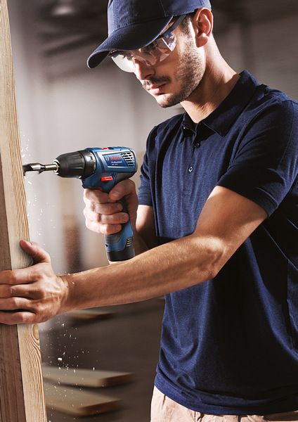 บุคคลที่สวมอุปกรณ์ความปลอดภัยกำลังเจาะรูในแผ่นไม้.