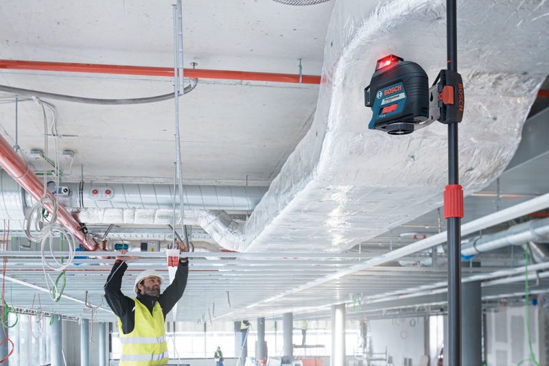 บุคคลที่สวมอุปกรณ์ด้านความปลอดภัยกำลังจัดตำแหน่งโครงเพดานโดยใช้เครื่องมือปรับระดับเลเซอร์.