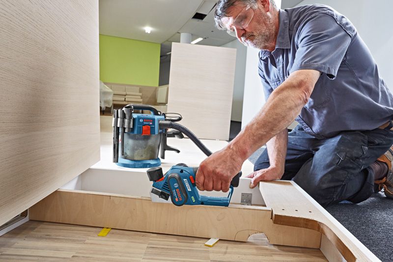 ผู้ที่สวมอุปกรณ์ด้านความปลอดภัยใช้เครื่องไสไม้แบบไร้สายในการขัดแผ่นไม้ให้เรียบ.