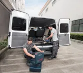 คนงานสองคนใกล้รถตู้เปิดจัดระเบียบเครื่องมือและใช้เครื่องดูดฝุ่นแบบไร้สาย.