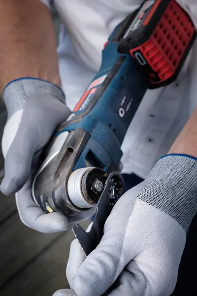บุคคลที่สวมอุปกรณ์ด้านความปลอดภัยกำลังติดใบมีดตัดเข้ากับเครื่องมือไฟฟ้าไร้สาย.