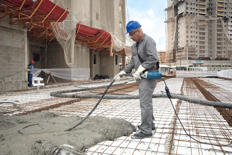 บุคคลที่สวมอุปกรณ์ด้านความปลอดภัยใช้เครื่องสั่นคอนกรีตบนไซต์ก่อสร้าง.