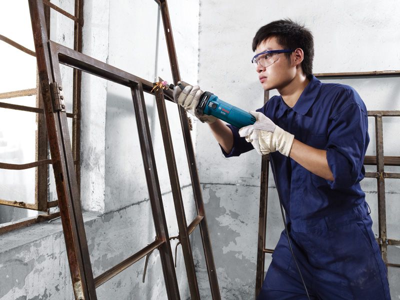 บุคคลที่สวมอุปกรณ์ป้องกันความปลอดภัยกำลังขัดกรอบหน้าต่างโลหะด้วยเครื่องขัดแบบตรง