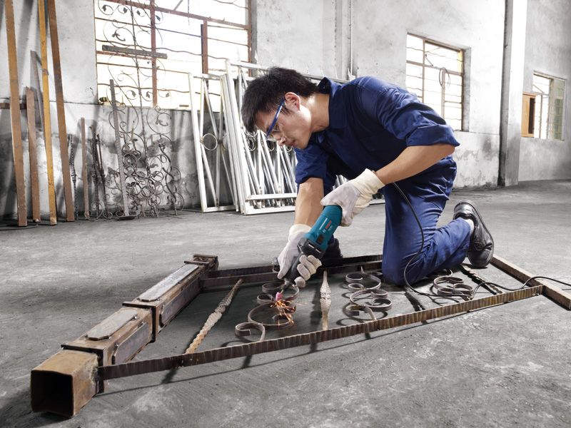 บุคคลที่สวมอุปกรณ์ความปลอดภัยกำลังขัดโลหะบนโครงประตู ทำให้เกิดประกายไฟ