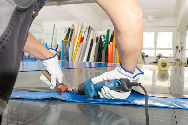 ผู้ที่สวมอุปกรณ์ด้านความปลอดภัยกำลังเชื่อมแผ่นพลาสติกโดยใช้ปืนความร้อน