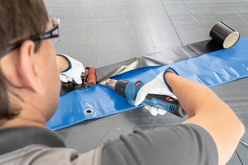 บุคคลที่สวมอุปกรณ์ด้านความปลอดภัยใช้ปืนความร้อนเพื่อปิดผนึกแผ่นพลาสติก