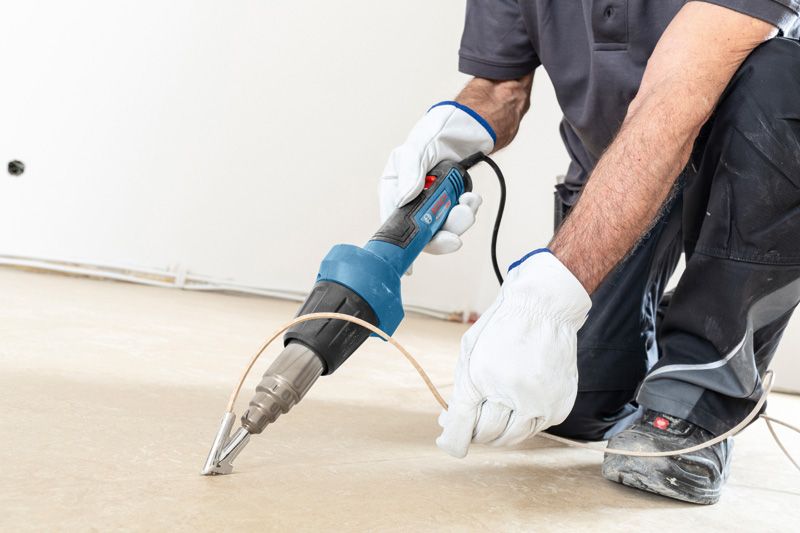 บุคคลที่สวมอุปกรณ์ด้านความปลอดภัยใช้ปืนความร้อนในการเชื่อมพื้น