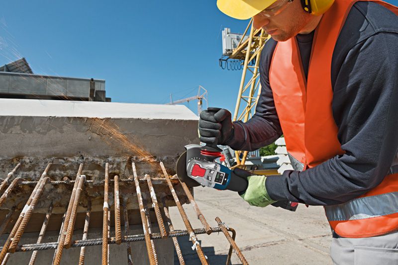 บุคคลที่สวมอุปกรณ์ความปลอดภัยกำลังตัดเหล็กเส้นที่เป็นสนิมด้วยเครื่องเจียรที่ไซต์ก่อสร้าง