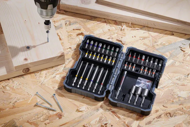 ชุดสว่านวางอยู่บนพื้นไม้อัดข้างๆ สกรูและแผ่นไม้