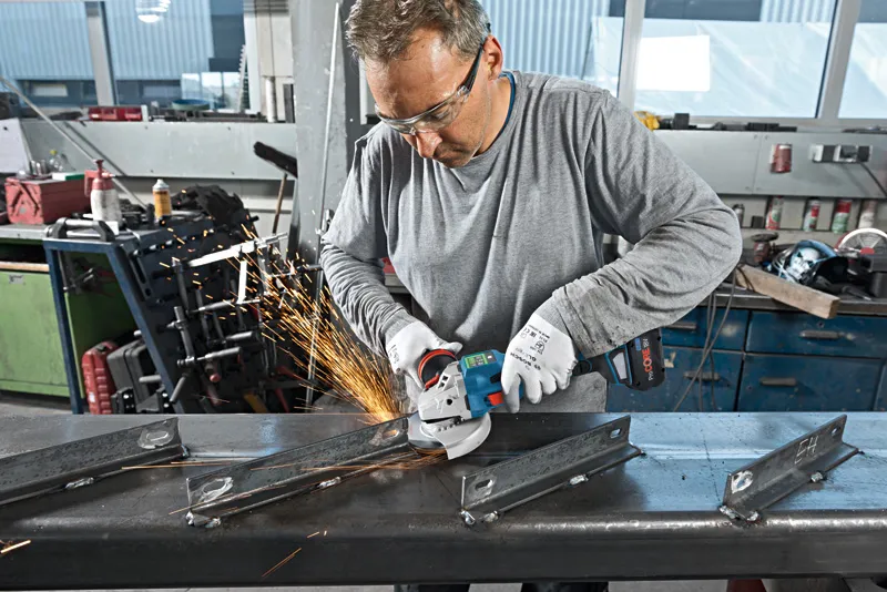 บุคคลที่สวมอุปกรณ์ด้านความปลอดภัยใช้เครื่องเจียรตัดคานโลหะ.