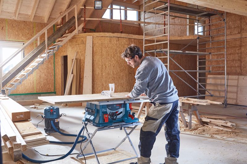 ผู้ใช้งานเลื่อยโต๊ะตัดไม้ในอาคารที่สร้างเสร็จเพียงบางส่วน.