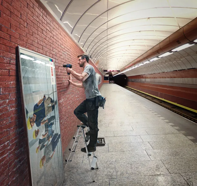 คนกำลังใช้สว่านไร้สายในการยึดกรอบบนผนังอิฐในสถานีรถไฟใต้ดิน.