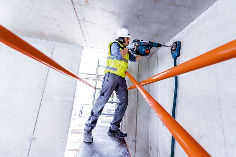 บุคคลที่สวมอุปกรณ์ความปลอดภัยกำลังเจาะฝ้าเพดานคอนกรีตด้วยสว่านโรตารี่